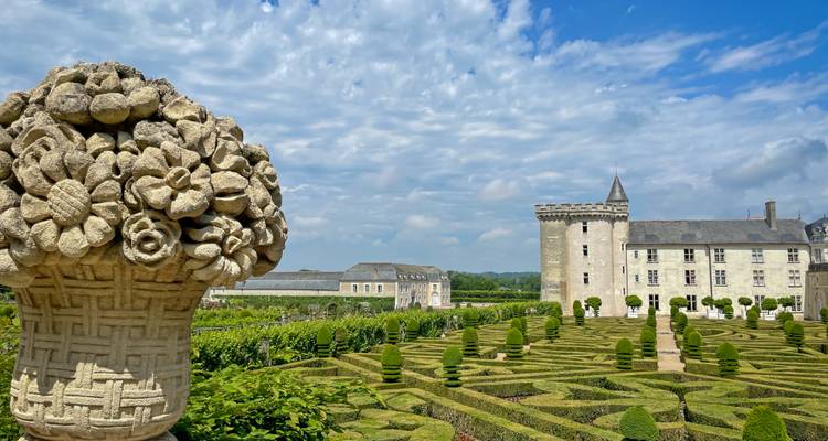 Elegantes jardines formales con setos recortados que conducen a un château de piedra bajo un cielo azul