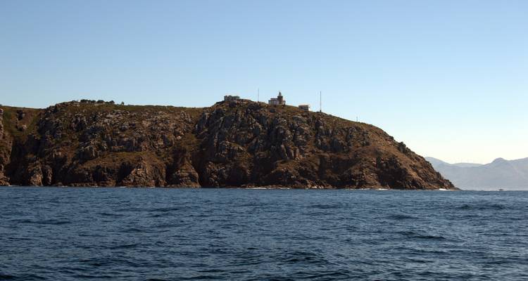 Eine Küstenklippe mit einem Gebäude oben drauf, umgeben vom Meer unter einem klaren Himmel.