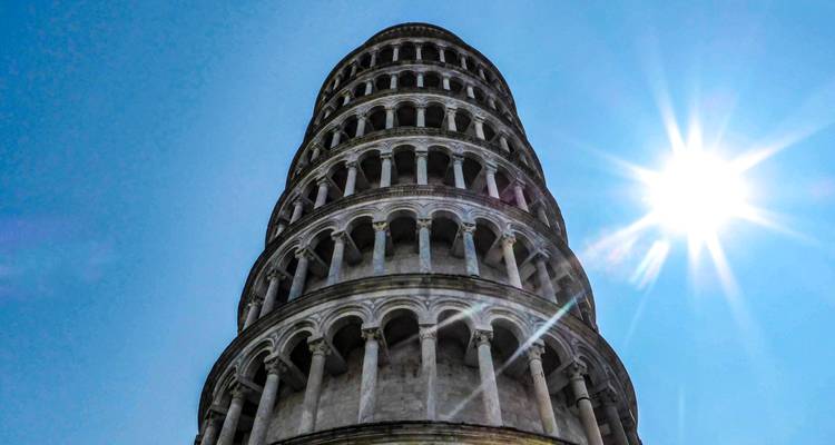 Aufwärtsblick auf den Schiefen Turm von Pisa vor einem hellen Himmel mit einem starken Sonnenstrahlen-Effekt.