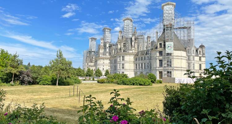 Vue latérale du château de Chambord sous échafaudage de restauration, encadrée par les jardins