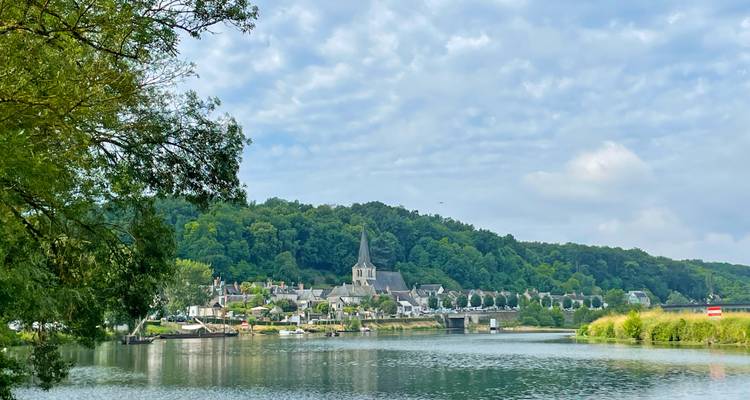 Village paisible au bord de la rivière avec clocher d'église en pierre adossé à des collines verdoyantes