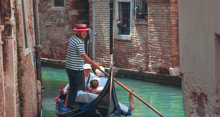Un gondolero dirigiendo una góndola a través de un estrecho canal veneciano.