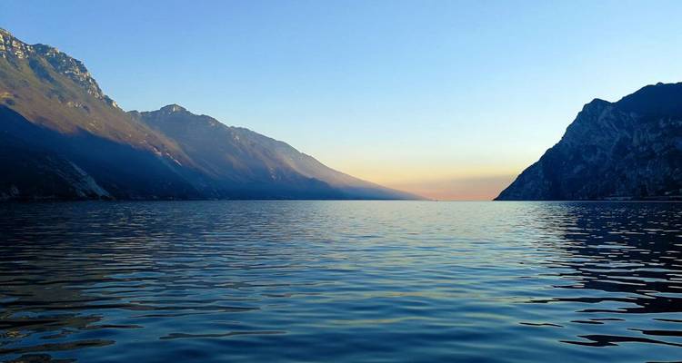 Las aguas tranquilas del lago reflejan siluetas de montañas al atardecer con un cielo de suave degradado.