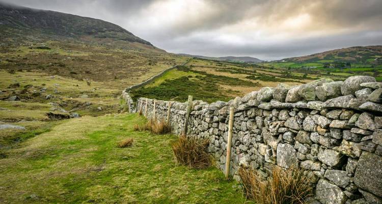 Muro de piedra antiguo serpenteando a través de un páramo azotado por el viento bajo cielos espectaculares.