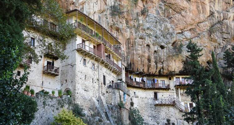 Un monastère à flanc de falaise construit dans la paroi rocheuse avec de la végétation environnante.