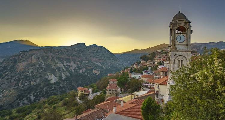 Une vue pittoresque d'un village avec un clocher, des montagnes et un coucher de soleil.