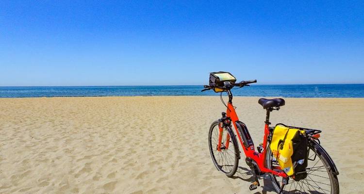 Fahrrad geparkt an einem sandigen Strand mit klarem blauen Himmel.