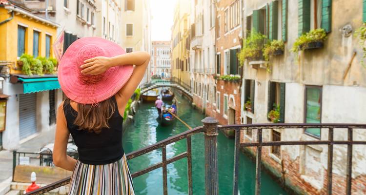 Frau mit einem rosa Hut mit Blick auf einen Kanal mit Gondeln in Venedig.