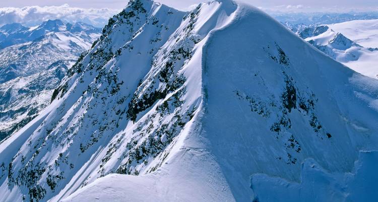 Een steile, met sneeuw bedekte bergkam met een blauwe lucht.