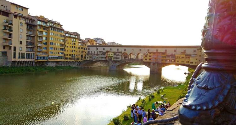 Menschen versammelten sich in der Nähe eines Flusses mit einer historischen Brücke im Hintergrund.