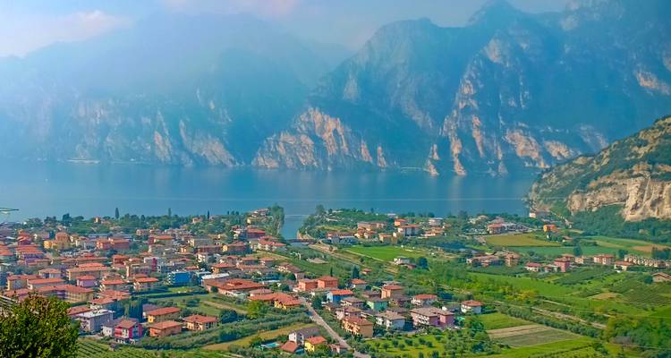 Vista elevada sobre un pueblo a orillas del lago con campos de cultivo en mosaico respaldados por acantilados de piedra caliza empinados al otro lado del agua.
