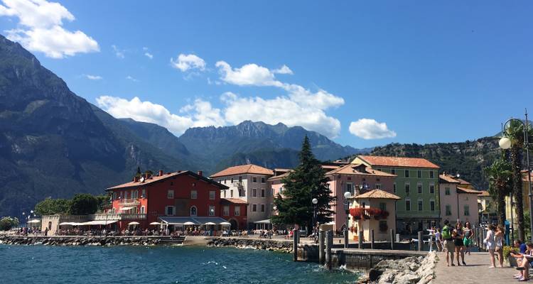 Bunte Gebäude entlang einer Seepromenade mit Bergen im Hintergrund.
