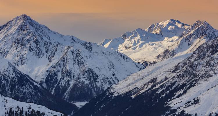 Cordillera alpina brillando en rosa y oro al atardecer con crestas nevadas y un cielo pastel suave.