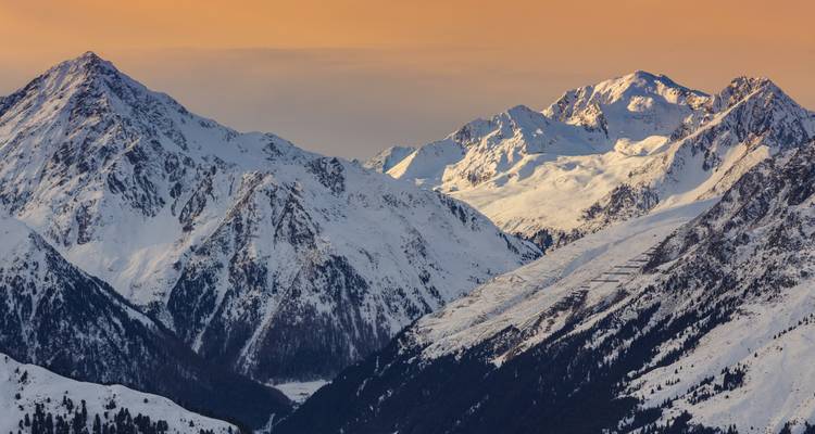 Picos alpinos nevados brillando bajo un cielo de atardecer anaranjado.