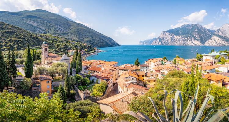 Vue panoramique d'un village italien au bord d'un lac avec des montagnes en arrière-plan.