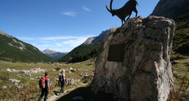 Deux randonneurs s'approchant d'une statue de bouquetin sur un rocher.