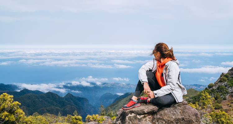 Mujer sentada en una roca, contemplando un valle.