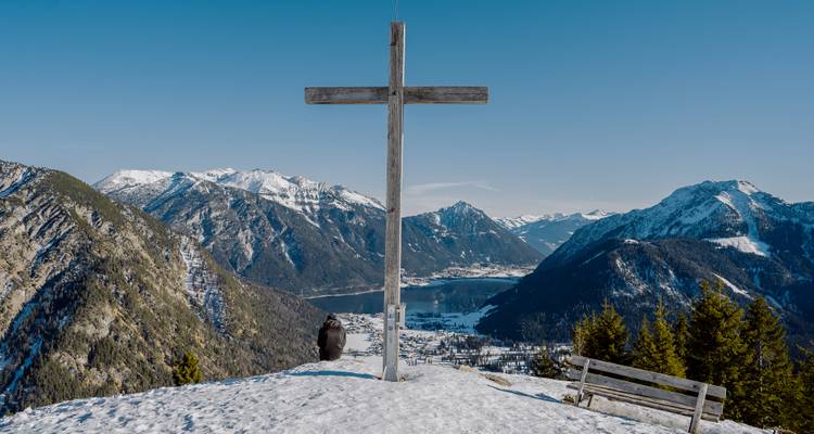 Croix sur un sommet de montagne avec vue sur un lac et des montagnes.