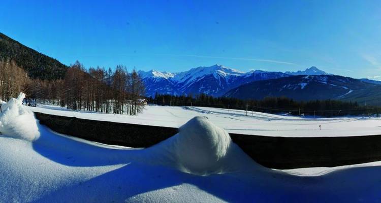 Panoramablick auf eine verschneite Landschaft mit Bergen und Bäumen im Hintergrund.