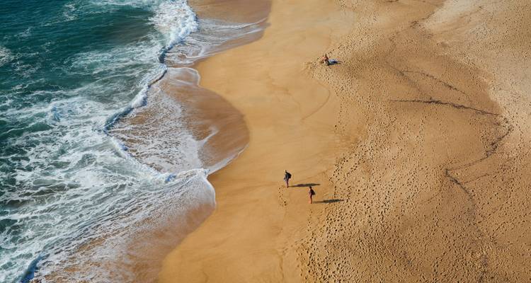 Plage avec vagues océaniques et personnes profitant du sable.
