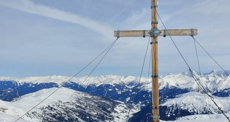 Sommet avec une grande croix en bois sur fond de montagnes enneigées.
