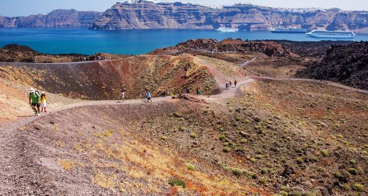 Tourists walking on a volcanic landscape with a sea view.