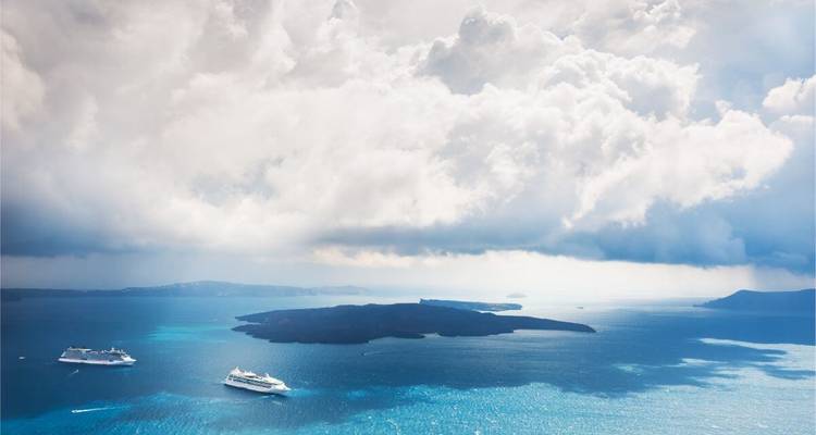 Aerial view of cruise ships near islands under dramatic sky and sea.