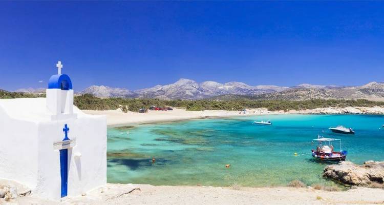 A white chapel by the sea with turquoise waters and boats.