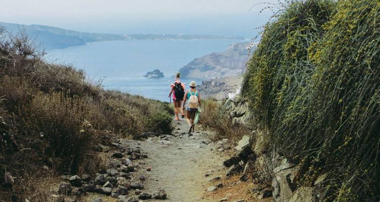 Two people walking on a mountain path with a sea view.