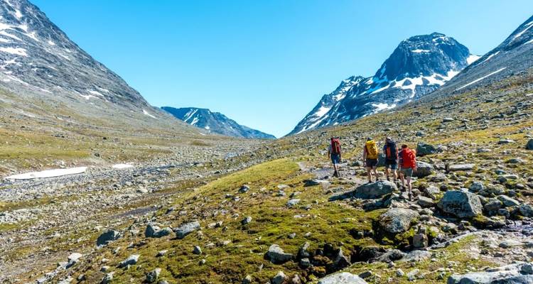 Randonneurs traversant un sentier montagneux rocheux sous un ciel dégagé.