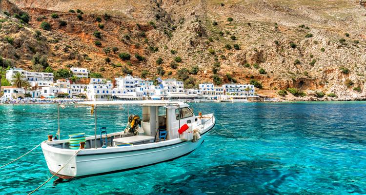 Boat on clear turquoise waters, with white buildings on shore.