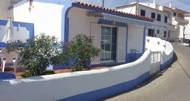 Petite maison blanche avec des garnitures bleues sur une rue.