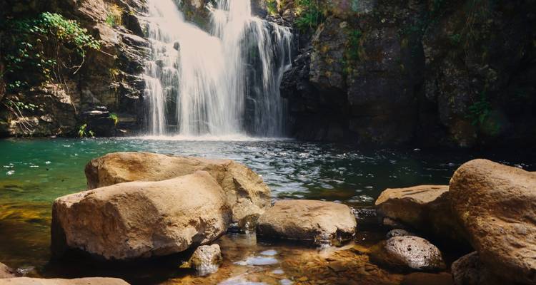 Großer Wasserfall, der in ein Becken mit Steinen drumherum fließt.