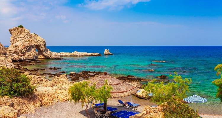 Beach with sun loungers, parasols, and a rocky coastline.