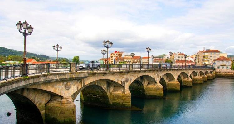 Pont de pierre au-dessus d'une rivière avec des bâtiments en arrière-plan, des voitures qui traversent.