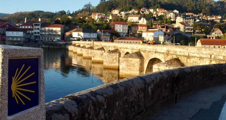 Pont de pierre au-dessus d'une rivière avec un arrière-plan résidentiel.