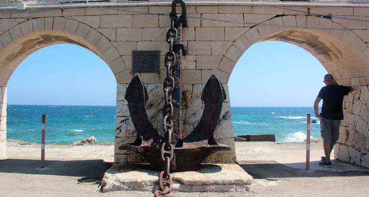 Groot anker sculptuur onder boogdoorgang bij de zee.
