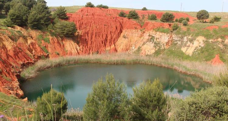 Canyon de terre rouge avec un lac vert et des arbres.