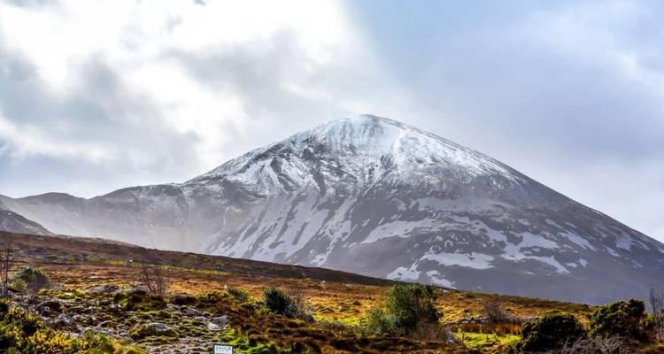 Croagh Patrick aux sommets enneigés s'élevant au-dessus des contreforts couverts de bruyère sous un ciel dégagé.