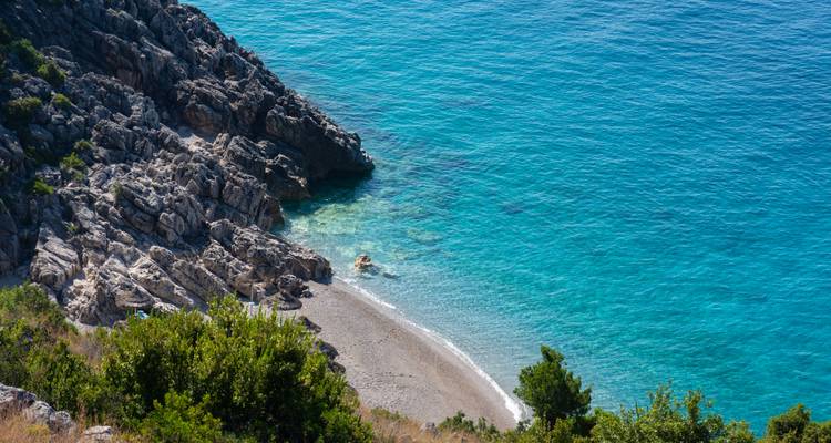 Une petite plage avec une eau bleue claire et un littoral rocheux.