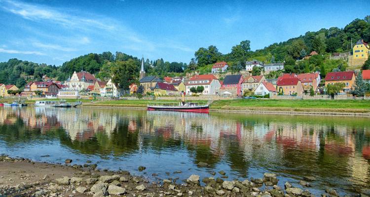 Ville riveraine colorée avec des collines vertes en arrière-plan.