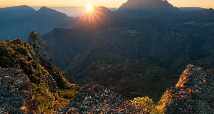 Dramatische zonsopgang die een sterrenuitbarsting over een ruige vulkanische cirque en verre bergtoppen werpt, gezien vanaf een klifrand.