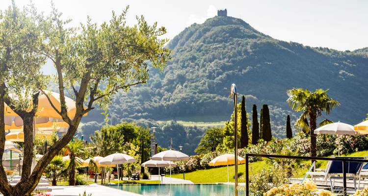 Une vue au bord de la piscine avec des parasols et une colline pittoresque au loin.