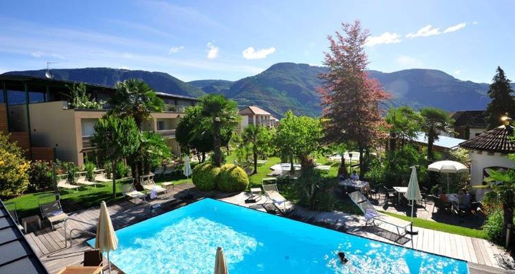 Un complexe hôtelier avec une piscine et une végétation luxuriante dans un décor de montagne.