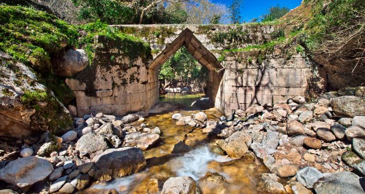 Un pont de pierre au-dessus d'un petit ruisseau entouré de rochers et de verdure.