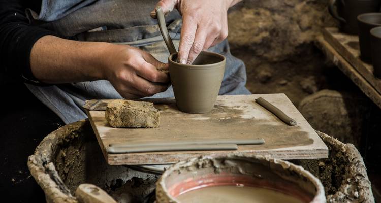 Personne sculptant un pot en argile sur un tour de potier.