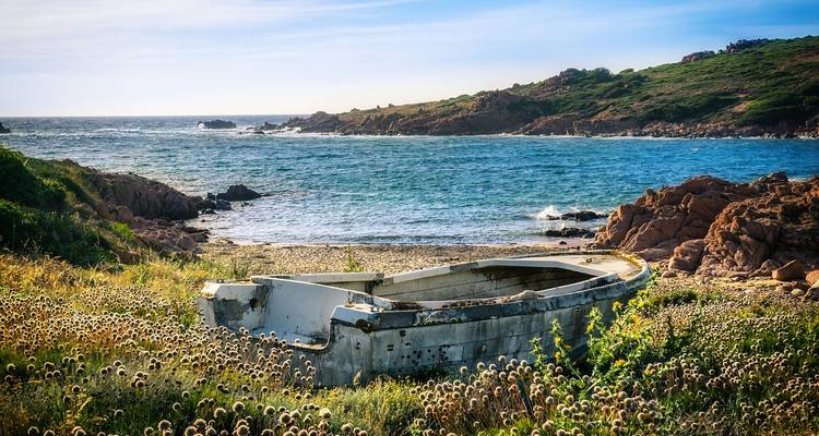 Abandoned boat on a beach with rocky coastline and sea in the background.
