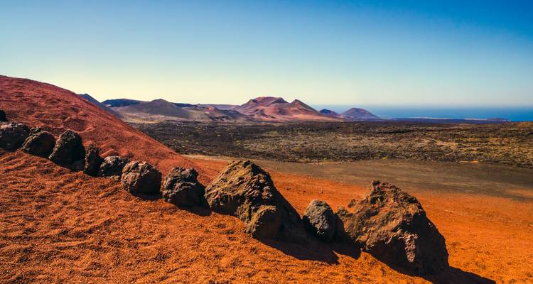 Red volcanic landscape with outcrops and blue sky.