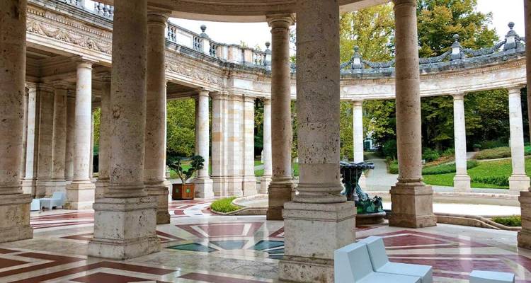 Shaded interior of Terme Tettuccio spa with marble columns and patterned floor looking onto gardens.