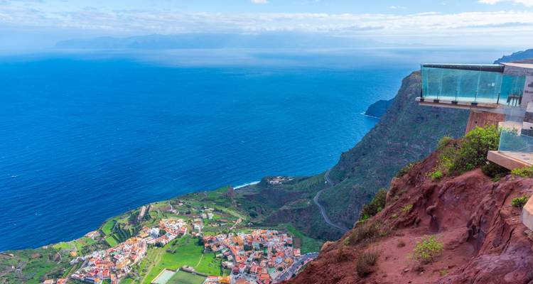 Vista costera con mirador de plataforma de cristal y mar al fondo.